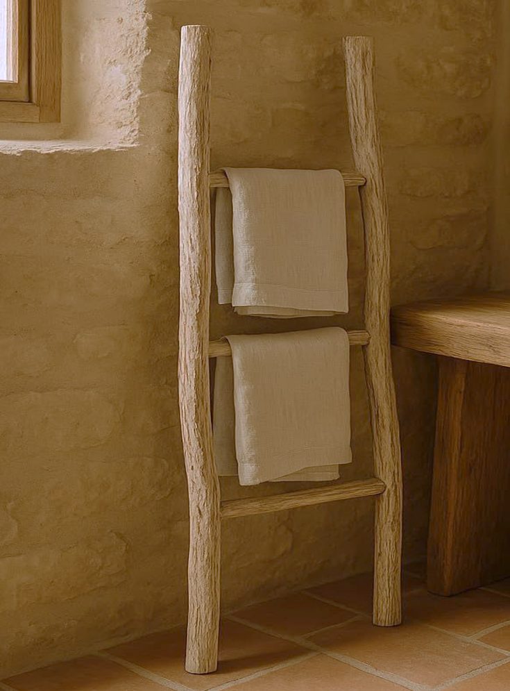 Linen towels on a rustic timber ladder against a limestone wall