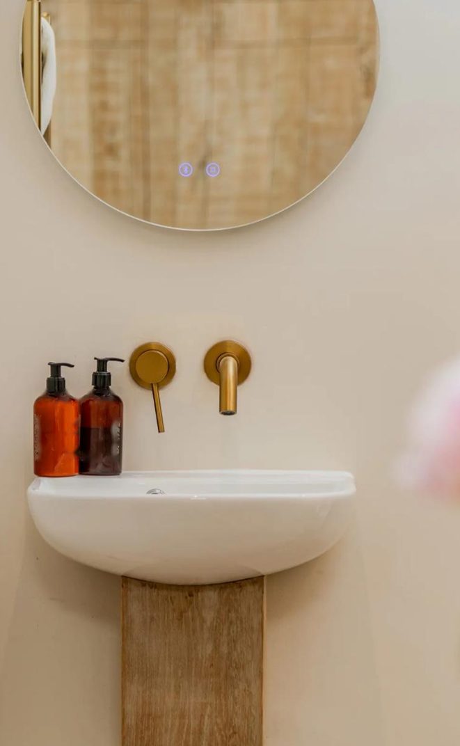 A wall-mounted basin with brushed brass taps and a round mirror